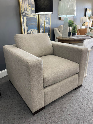 A beige upholstered chair with a high backrest and simple design, displayed in a showroom setting.