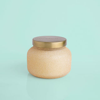 A 19oz Capri Blue Pumpkin Dulce Glam Signature Candle with a champagne glitter finish and a gold lid on a light green background.