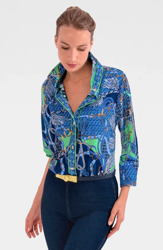 A woman wearing a colorful geometric patterned shirt with shiny brass buttons, styled with the sleeves rolled up to the elbows.