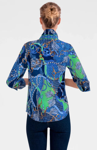 A woman wearing a colorful geometric patterned shirt with shiny brass buttons, styled with the sleeves rolled up to the elbows.