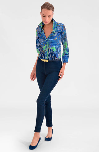 A woman wearing a colorful geometric patterned shirt with shiny brass buttons, styled with the sleeves rolled up to the elbows.