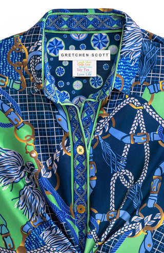 A woman wearing a colorful geometric patterned shirt with shiny brass buttons, styled with the sleeves rolled up to the elbows.