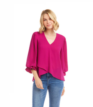 Woman wearing a bright pink blouse and blue jeans on a white background. Karen Kane V neck Layered Sleeve Asymmetric Top, Magenta