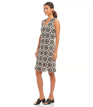 A model wearing a sleeveless knee-length crochet shift dress with a V-neck and scalloped hem, in black and white.