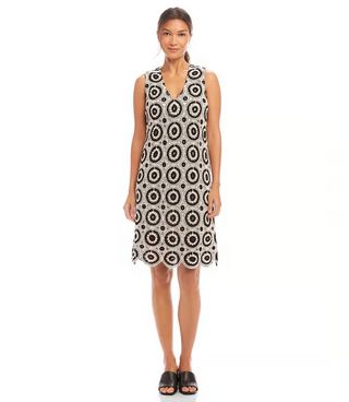 A model wearing a sleeveless knee-length crochet shift dress with a V-neck and scalloped hem, in black and white.
