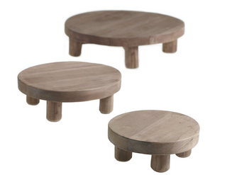 Two round wooden stands with a simple, modern design, featuring a flat surface on top and three curved legs. Large Tejano Stand.