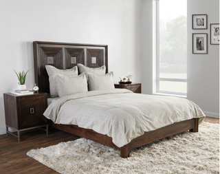A taupe-colored duvet cover on a bed in a room with a wooden headboard and a white carpet.