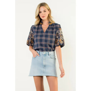 Woman wearing a THML navy plaid shirt with floral embroidered sleeves and a denim skirt on a white background