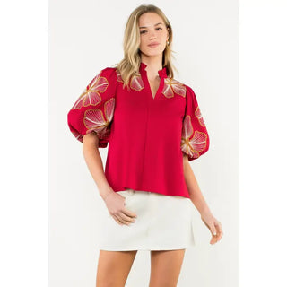 Woman wearing a THML burgundy blouse with floral sleeves on a white background