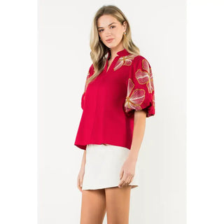 Woman wearing a THML burgundy blouse with floral sleeves on a white background