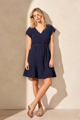 A woman wearing a navy A-line dress with cap sleeves, a V-neckline, functional pockets, and an adjustable sash at the waist.