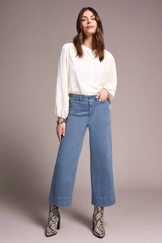 Woman wearing a white blouse and blue jeans against a plain background