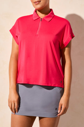 A woman wearing a pink tribal dolman polo top with a collar, paired with a gray skirt.