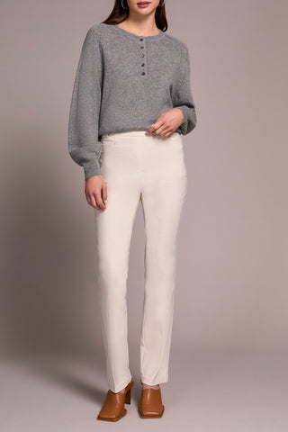 Person wearing a gray sweater and white pants against a plain background