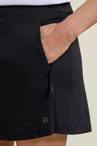 A woman wearing a white sleeveless top and black skort with pockets.