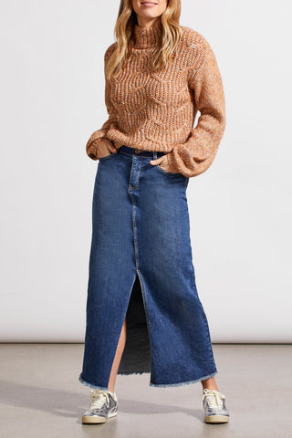 A woman wearing an almond-colored funnel neck oversized sweater paired with a long denim skirt.