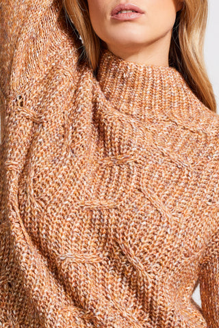 A woman wearing an almond-colored funnel neck oversized sweater paired with a long denim skirt.