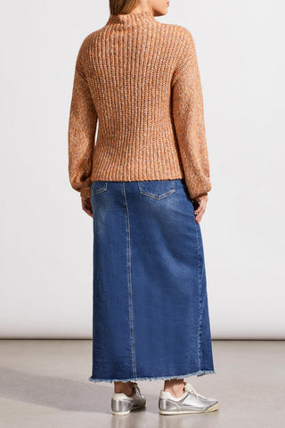A woman wearing an almond-colored funnel neck oversized sweater paired with a long denim skirt.