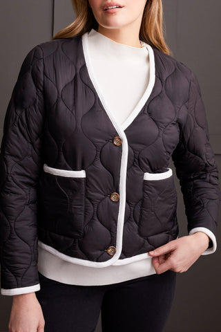 A woman wearing a black long sleeve button front puffer jacket with a round neckline and two-way front pockets, paired with a white top and black trousers.