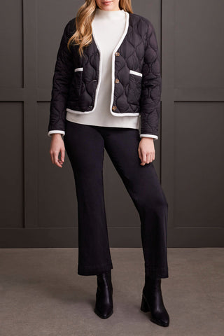 A woman wearing a black long sleeve button front puffer jacket with a round neckline and two-way front pockets, paired with a white top and black trousers.