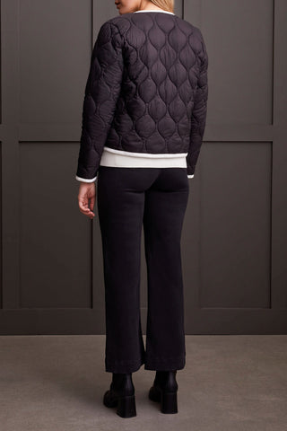 A woman wearing a black long sleeve button front puffer jacket with a round neckline and two-way front pockets, paired with a white top and black trousers.