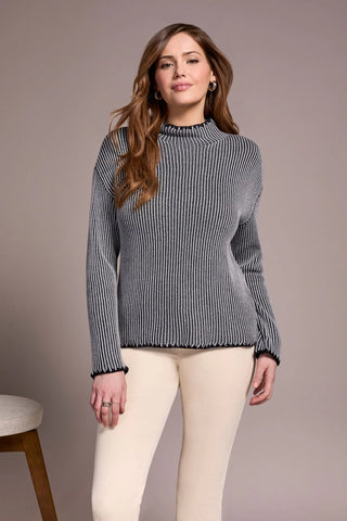 Woman wearing a gray ribbed sweater and white pants against a plain background
