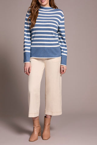 Person wearing a blue and white striped sweater with beige pants on a plain background
