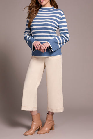 Person wearing a blue and white striped sweater with beige pants and boots on a plain background