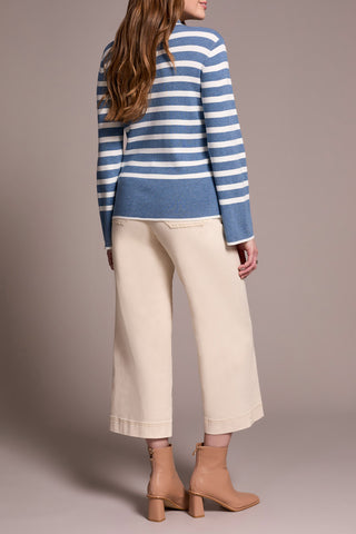 Person wearing a blue and white striped sweater with beige pants on a plain background