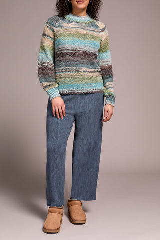 Person wearing a striped sweater and jeans with a neutral background.