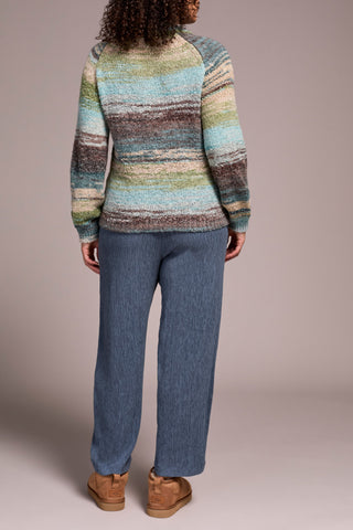 Person wearing a multicolored sweater and blue jeans on a plain background