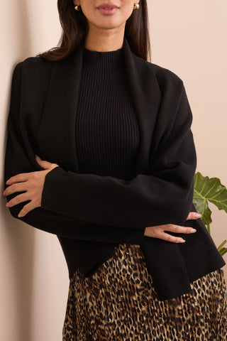 Woman wearing a black cardigan over a black top with leopard print pants against a beige background