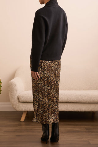 Person wearing a black turtleneck and leopard print skirt standing in a room with a beige sofa.