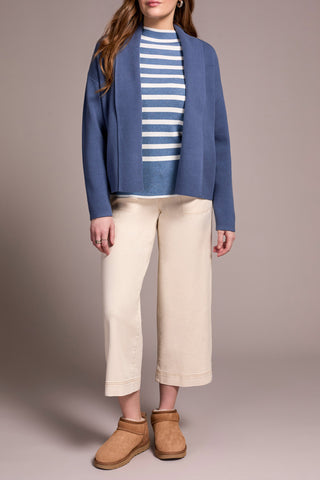 Person wearing a blue jacket, striped shirt, beige pants, and brown boots on a plain background