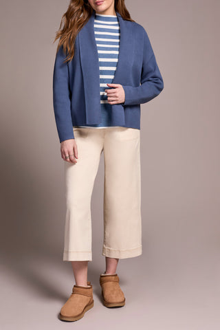 Person wearing a blue cardigan, striped shirt, beige pants, and brown boots on a plain background