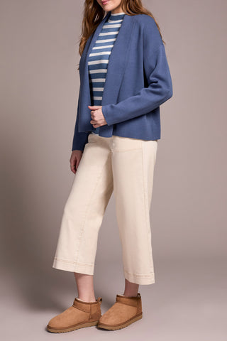 Person wearing a blue cardigan, striped shirt, beige pants, and brown shoes on a plain background