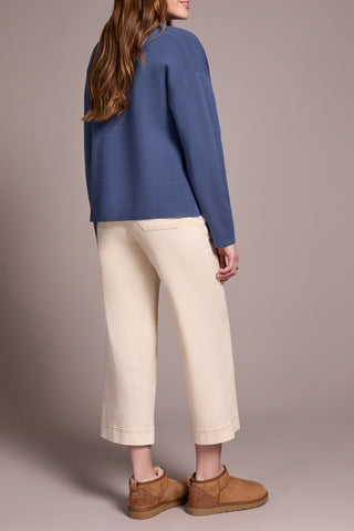 Person wearing a blue sweater and beige pants against a neutral background