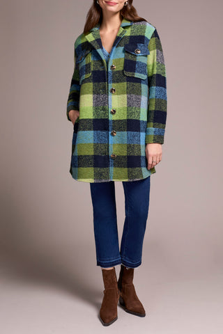 Person wearing a green and blue plaid coat with blue jeans and brown boots on a beige background