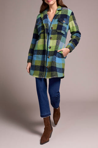 Person wearing a plaid coat with blue jeans and brown boots on a neutral background