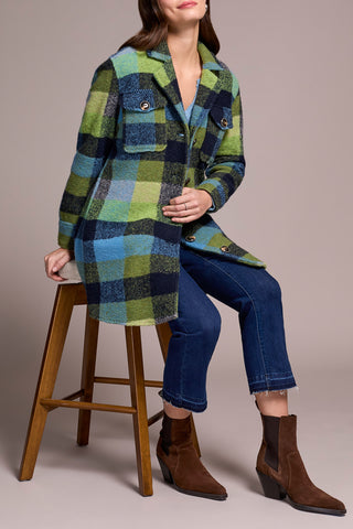 Person wearing a plaid coat, jeans, and brown boots sitting on a wooden stool against a plain background.