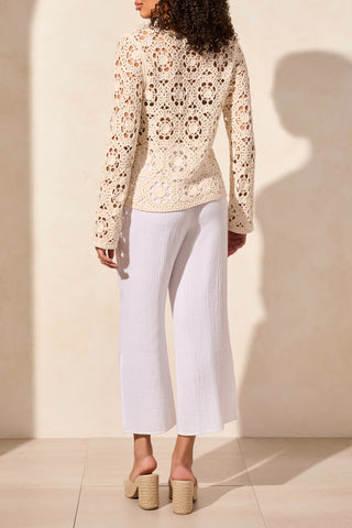 A woman wearing a beige, open fancy crochet v-neck bell sleeve sweater in a store.