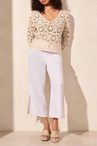 A woman wearing a beige, open fancy crochet v-neck bell sleeve sweater in a store.
