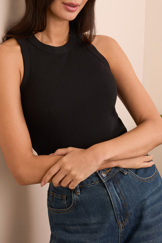 A woman wearing a black racer back tank top with a ribbed texture, paired with blue jeans.