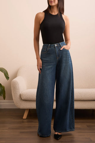 A woman wearing a black racer back tank top with a ribbed texture, paired with blue jeans.