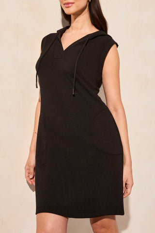 A woman standing wearing a black sleeveless hooded dress with pockets and a V-neckline.