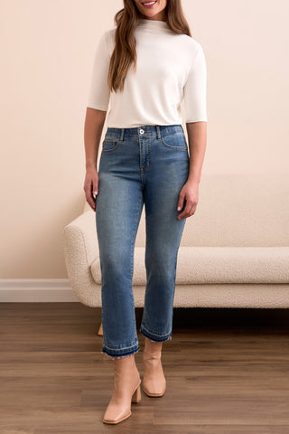 Woman wearing a white top and blue jeans standing in a room with a beige couch.