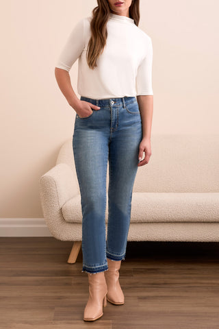 Woman wearing a white top and blue jeans standing in a room with a beige couch.
