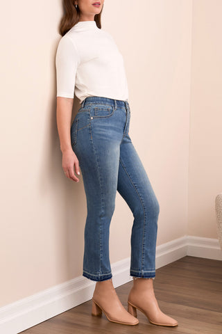Woman wearing blue jeans and a white top against a beige wall.
