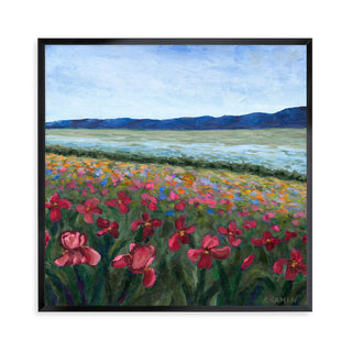A framed artwork featuring a vibrant floral pattern with a landscape background, including a body of water and mountains.