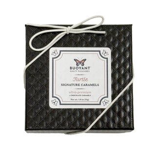 Black gift box with a label for Turtle Signature Caramels on a white background